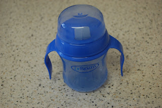 A Dr Brown's Soft Spout Trainer Cup with two handles and a lid sits on a speckled worktop, designed to promote a natural flow for easy sipping.