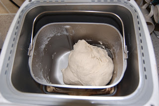 A dough ball sits inside the metal mixing tin of a Panasonic bread maker, ready to be kneaded or baked. The SD-254 bread machine’s interior and some flour dust on the sides are also visible.