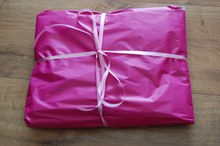 A rectangular present wrapped in bright pink paper with a matching pink ribbon, reminiscent of a Pink Lining Mum on the Run Bag, sits elegantly on a wooden surface.