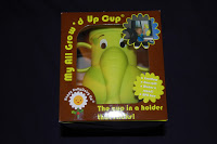 A boxed yellow elephant-shaped toddler cup labelled "My All Grow'd Up Cup," with features listed on the packaging, sits against a dark background.