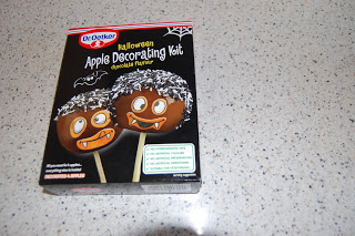 A box of Dr. Oetker Halloween Apple Decorating Kit with chocolate flavour sits on a speckled worktop. The Apple Decorating Kit shows two apple pops with vampire faces and fun Halloween-themed graphics.