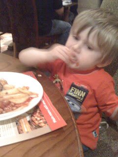 A young child with blond hair wearing a red "Finn" shirt sits at a table in the Turnpike Brewers Fayre restaurant, eating food with his hands from a plate of chips and beans.