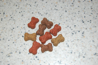 A small pile of bone-shaped dog biscuits, including Wagg Training Treats, in brown, red, and tan colours rests on a speckled worktop.