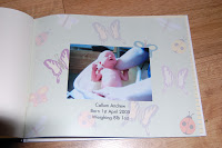 A Snapfish photo album page featuring a newborn baby being held, adorned with butterfly and ladybird illustrations, plus text below the photo sharing the baby's name, birth date, and weight.