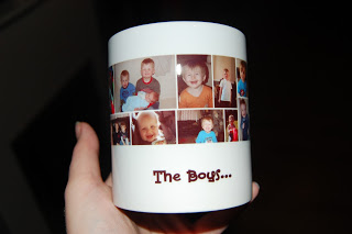 A hand holds a white mug from Snapfish, decorated with childhood photos of boys and the text "The Boys..." printed below the pictures.