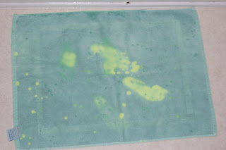 A light blue-green Cuddledry towel with several bright yellow stains and spots is laid flat on a light-coloured surface.