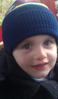 A young child with blue eyes is wearing a navy blue knitted hat and a dark coat, smiling slightly and looking at the camera—captured as if for an HTC Flyer review. The background is blurred with hints of red and green.