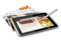 A digital tablet with a stylus, reminiscent of those in an HTC Flyer review, displays a recipe and food photos, with several printed recipe pages or magazines partially visible underneath it.