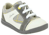 A children's trainer from Clarks with white and grey panels, yellow stitching accents, a chequered pattern on the sides, white laces, and a grey sole—perfect for spring style or summer adventures. The "Clarks" logo is visible on the side.