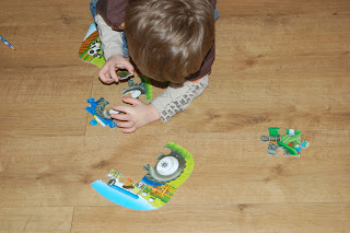 A young child with brown hair is sitting on a wooden floor, assembling a colourful jigsaw puzzle. Several pieces from the Jiqsaw Puzzles collection are scattered around as the child focuses on fitting two together.