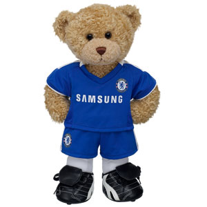 A Curly Teddy plush bear stands upright in a blue Chelsea football kit with "Samsung" logo, white socks, and black and white football boots, perfect for any football fan against a crisp white background.