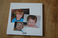 A white Pixum Photo Book rests on a wooden surface, featuring three pictures of a young boy with fair hair, smiling in two photos and looking at the camera in the third.