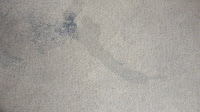 A close-up of a light-coloured wall with a faint, irregular dark stain and smudges, creating a subtle abstract pattern on the surface—ideal for demonstrating the effectiveness of Rug Doctor Urine Eliminator.