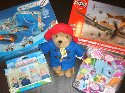 A collection of toys, including a Paddington Bear soft toy, metal model construction kit, Airfix Spitfire aeroplane model, My Little Pony Rainbow Dash figure, and Sylvanian Families pig family set—no batteries included. Great for competition and creative play!.