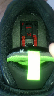 A small toy car is placed inside the heel of a black trainer, which features a bright yellow-green pull tab on the tongue—perfect for Back To School Clarks style.