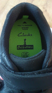 Close-up of the inside heel of a black Clarks shoe, featuring a bright green insole with Clarks and Jack Nano logos, plus size info: 11½F, 29½M—perfect for Back To School essentials.