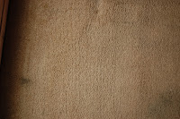 A close-up of a beige carpet with some darker and lighter areas, showing slight discolouration and wear—perfect for refreshing with a Rug Doctor carpet cleaner.