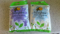 Two packs of Bizzybee Gloves moisturising gloves are shown on a worktop. The left pack has a purple flower and the right has a blue flower, both featuring a smiling bee cartoon above the brand name.