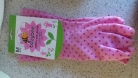 A pair of pink gardening gloves with small red polka dots, labelled "Bizzybee Gloves" on a green and white tag, lying on a speckled worktop—ideal for gardening or paired with your favourite cleaning products.