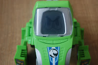 A close-up of a green Switch & Go Dinos toy vehicle by Vtech, featuring a blue and white design with a black dinosaur logo on the front, placed on a wooden surface.