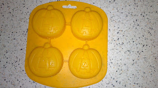 A yellow silicone mould from Poundland with four pumpkin-shaped cavities, each featuring a jack-o'-lantern face, sits on a white speckled worktop—perfect for Hallowe'en treats.