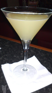 A pale yellow cocktail from Frankie & Benny's is served in a martini glass, placed on a white serviette atop a dark countertop.