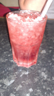 A glass filled with a pink-red iced cocktail and a straw, sitting on a dark, speckled worktop at Frankie & Benny's.