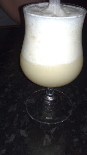 A frothy, light yellow cocktail served in a stemmed glass sits on a dark worktop—perfect for a night out at Frankie & Benny’s.
