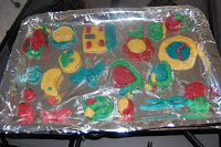 Colourful, playdough-like shapes made from Yummy Dough in red, yellow, green, and blue are arranged on a foil-lined baking tray, making fun activities for children with various abstract and geometric designs.