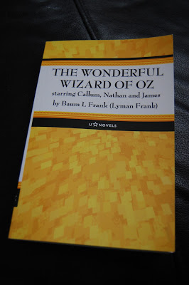 A yellow U Star Novels book titled "The Wonderful Wizard of Oz starring Callum, Nathan and James by Baum L. Frank (Lyman Frank)" rests on a dark surface, ready for your next great review.