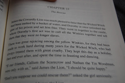 A close-up of an open book, similar to those from U Star Novels, showing part of Chapter 13 titled "The Rescue," where the Cowardly Lion, Dorothy, the Wicked Witch, Winkies, and others celebrate freedom.