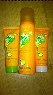 Three orange and green tubes and a spray bottle of Oriflame Feet Up products—Foot Scrub, Foot Spray, and Foot Cream—are displayed upright on a wooden surface. Pamper your feet with the revitalising Oriflame Feet Up collection.