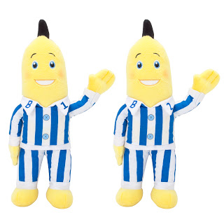 Two smiling yellow banana plush toys in blue and white striped pyjamas, labelled "B1" and "B2." With raised arms and black hair tufts, they're perfect Christmas gift ideas for younger children who love cuddly mates.