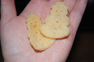 A hand holding two snowman-shaped snacks, one larger and one smaller, against a dark background—perfect festive treats for fans of Pom-Bears and other playful snacks.