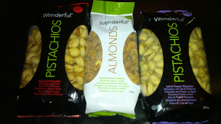 Four bags of Wonderful Pistachios and Wonderful Almonds on a dark surface: pistachios on the sides and almonds, in white and green packaging, in the centre. The classic black branding stands out across all four bags.