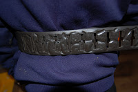A close-up of a wide, dark Magic Sapstone Belt with engraved designs, worn over a dark blue garment from the Holopax Set. The background is out of focus.