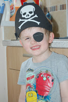 A young child wearing a pirate hat with a skull and crossbones and a black eye patch, smiling in a kitchen, ready for a Pirate Party.