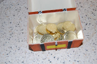 A small open treasure chest filled with gold coins sits on a speckled worktop, perfect as a centrepiece for your next Pirate Party.