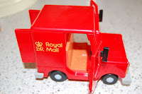 A small red Classic Vehicle Toy Royal Mail delivery van with open doors, showing an empty orange interior, placed on a speckled worktop.