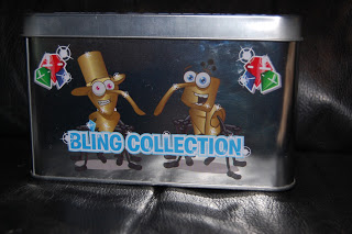 A Bling Collector Tin labelled "BLING COLLECTION" features two cartoon Bin Weevils wearing glasses and accessories, with colourful icons and shiny footballs in the background.