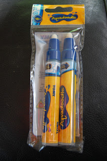 A pack of two TOMY Aquadoodle water pens in blue and yellow plastic, sealed in clear packaging, placed on a dark surface. Perfect for use with Aquadoodle drawing mats or to pair with the Jungle Magic Sounds Aquadoodle set.