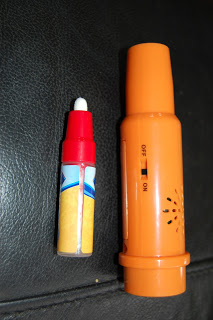 A small red and white dropper bottle is placed next to an orange Tomy Jungle Magic Sounds Aquadoodle device with a slider switch labelled "NO" and "350" on a black surface.