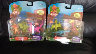 Two packs of small colourful dinosaur toys from the show "Dinosaur Train," each containing three dinosaurs, are displayed on a black surface. The packaging is bright with cartoon backgrounds—perfect for your next Dinosaur Train toy review.
