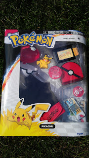 A Pokémon-themed toy set in packaging, featuring a Pikachu figure, two Poké Balls, accessories, and a cartoon image of Pikachu on the bottom left, displayed on grass—the perfect Pokémon Trainer Kit for any fan.