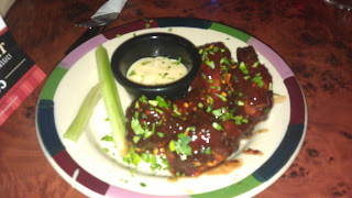A plate of saucy chicken wings garnished with herbs is served with celery sticks and a small pot of creamy dipping sauce—perfect for a special night at Frankie & Benny's.