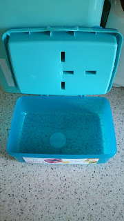 An open, empty blue plastic container with a hinged lid sits on a speckled worktop. Ideal for Back to School, its simple geometric features and small Asda label on the front make it both practical and stylish.
