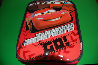 A red zip-fastened pencil case featuring a smiling animated racing car character from the film "Cars" with the text "Superteam Supercars GO!" on a green background—perfect for Back to School essentials from Gettingpersonal.co.uk.