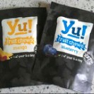 Two packets of Yu Snacks Fruit Chews are shown on a worktop—one mango with yellow accents, the other blueberry with blue. Both display fruit images and branding, perfect for your next snacks review.