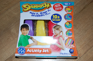 A Skwooshi Activity Set box featuring three colourful moulding compounds (yellow, purple, red) with images of a boy and girl playing. The box highlights "10+ activities," "20 fun colours," and includes activity ideas—perfect for your next review!.