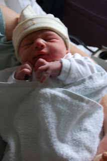 A newborn baby wrapped in a white blanket and wearing a striped hat is lying in someone’s arms, resting peacefully with eyes closed, unaware of the world and untouched by any feeling lost.